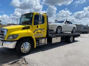 Yellow Flatbed Towing Truck Loaded with White Luxury Sedan Car