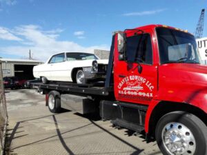 Red Chavez Towing Truck Loaded With White Vintage Car